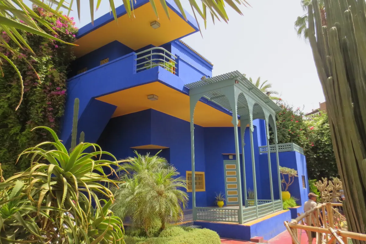 The blue Cubist villa of the Majorelle Garden with its yellow balcony ceiling, a pale green veranda and tall cacti beside it